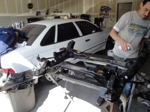 1989 Ford Taurus - A white 1989 Ford Taurus is parked in a garage while engine parts are being worked on in the foreground.