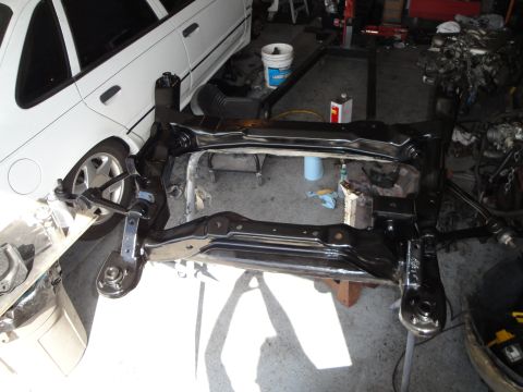 1989 Ford Taurus - Subframe and suspension parts are laid out in a garage, with a white car visible behind them.