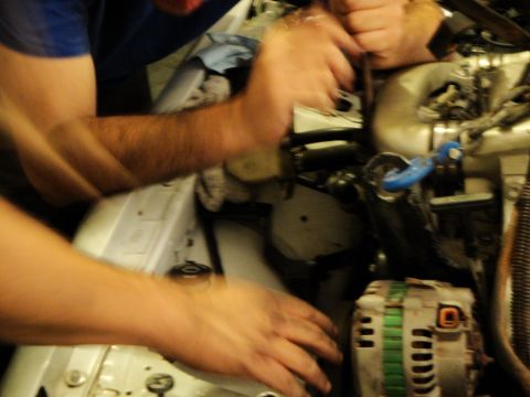 1989 Ford Taurus - Hands are busy working on the engine bay of a vehicle, focusing on the alternator and surrounding components.