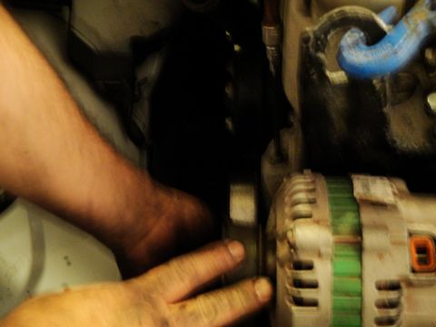 1989 Ford Taurus - Close-up view of hands manipulating engine parts, including an alternator.