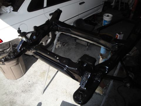 1989 Ford Taurus - A black front subframe assembly is shown, with a white car visible behind it.