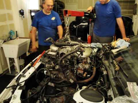 1989 Ford Taurus - Two men are working on removing the engine from a car using an engine hoist in a garage.
