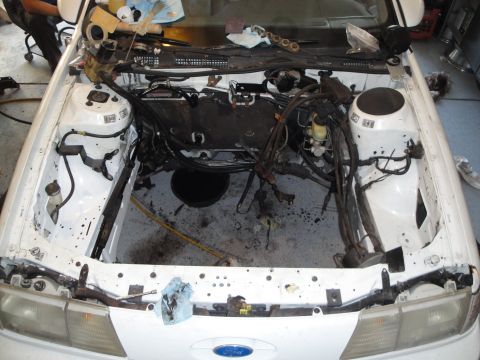 1989 Ford Taurus - The engine bay of a white 1989 Ford Taurus is shown with the engine removed, revealing exposed wiring and components.