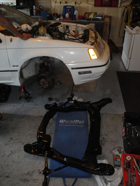 1989 Ford Taurus - Front view of a 1989 Ford Taurus undergoing engine work, with the engine removed and suspension components laid out.