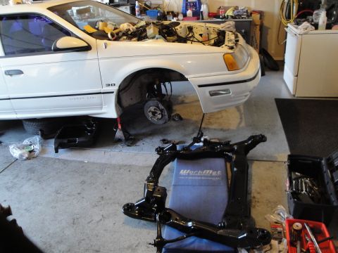 1989 Ford Taurus - A white 1989 Ford Taurus is shown with its engine compartment exposed and front subframe removed for repair.