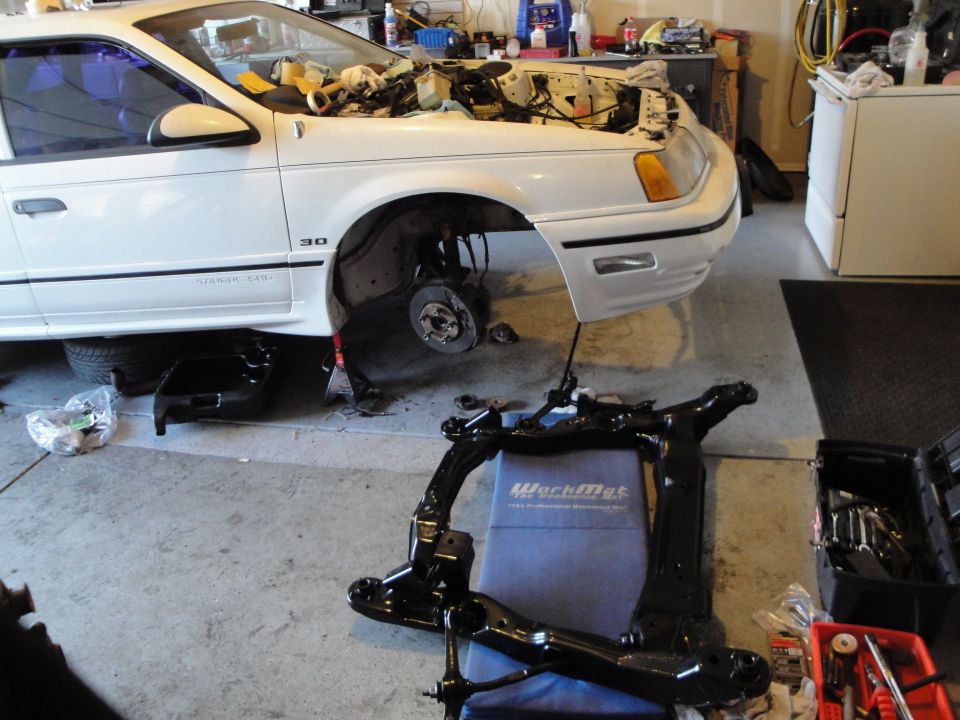 White 1989 Ford Taurus with hood open, front end disassembled, and subframe removed