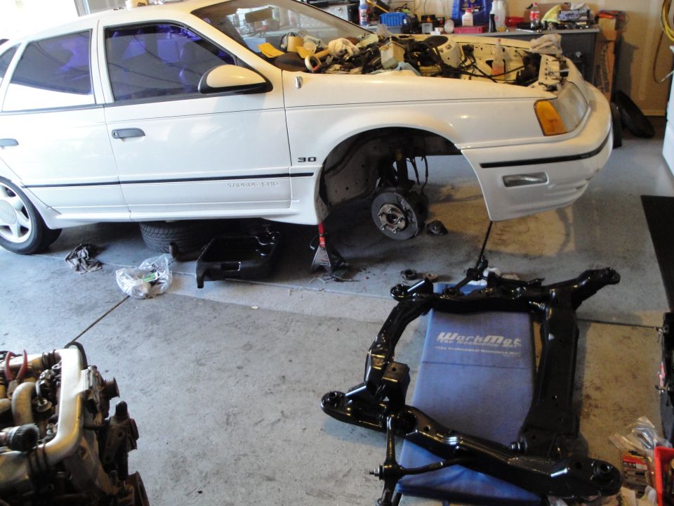white sedan with hood up, front end disassembled, parts on floor