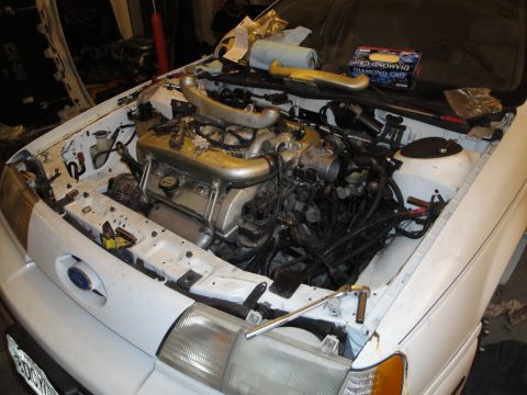 1989 Ford Taurus - The engine bay of a white 1989 Ford Taurus shows a large V6 engine with a turbocharger, indicating an engine swap.