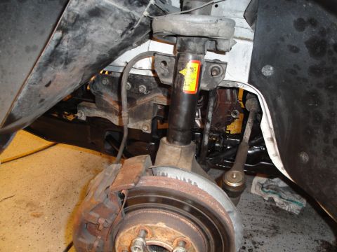 1989 Ford Taurus - Detail of a vehicle's front suspension and braking system, showing worn components and a yellow sticker on the shock.