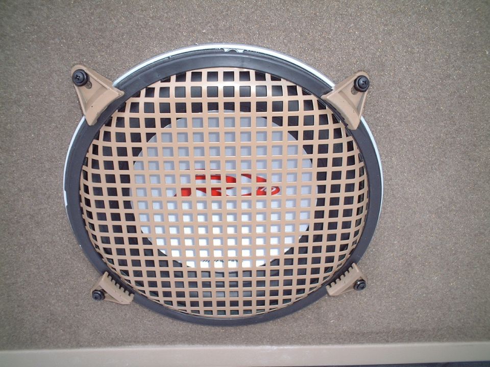 Round car speaker with tan lattice grille and four clips in a beige interior panel
