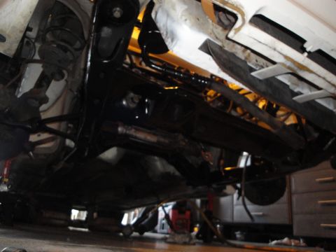 1989 Ford Taurus - Vehicle is raised on jack stands for undercarriage work, revealing suspension and exhaust systems.
