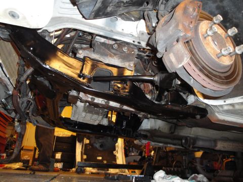 1989 Ford Taurus - The underside of a vehicle is shown, revealing its engine and suspension systems during a repair or modification.