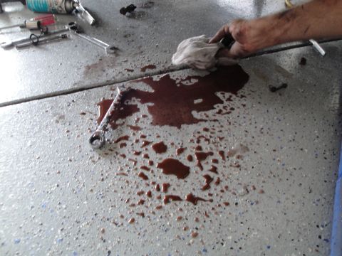 1989 Ford Taurus - A mechanic cleans up an engine oil spill on a speckled garage floor, surrounded by tools.