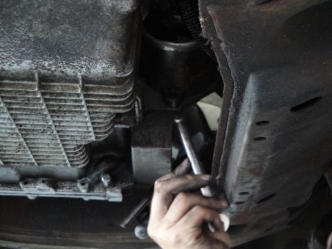 1989 Ford Taurus - Mechanic works on the underside of a vehicle, focusing on the engine oil pan and transmission.