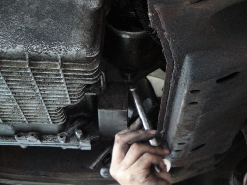 Close-up of a hand using a wrench on a car's engine oil pan and transmission housing