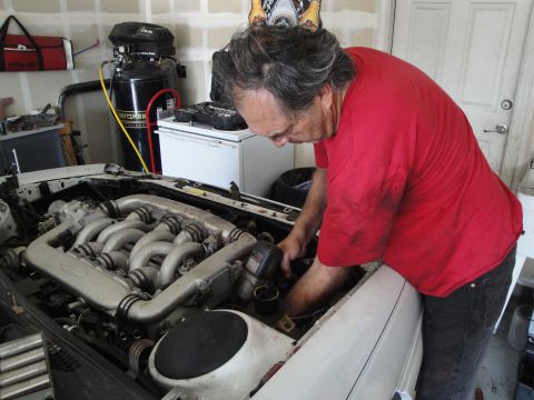 1989 Ford Taurus - A man performs maintenance on a car's engine, which has a distinctive V-shaped intake manifold.