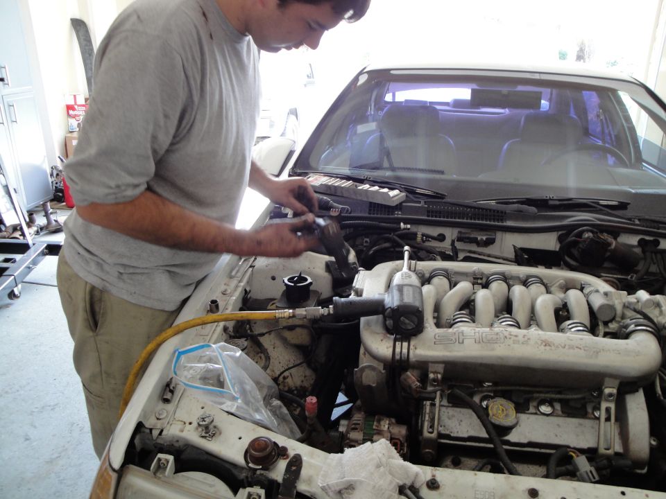Man in grey shirt works on white car engine with SHO intake manifold