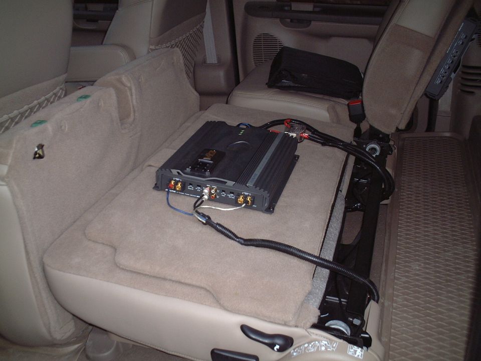 Black amplifier mounted on folded tan SUV seat with wiring