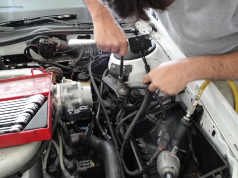1989 Ford Taurus - A person is using a socket wrench to work on a car's engine bay, with a red toolbox nearby.