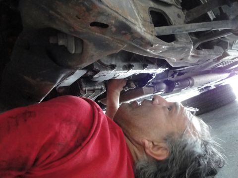 1989 Ford Taurus - A person works on the underside of a car, focusing on the engine components.