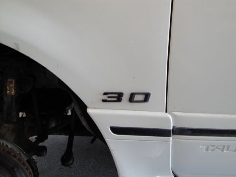 1989 Ford Taurus - A portion of a white vehicle's exterior shows a '30' emblem and part of the 'TAURUS' nameplate.