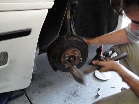 1989 Ford Taurus - Mechanic works on the brake rotor and hub assembly of a white vehicle.