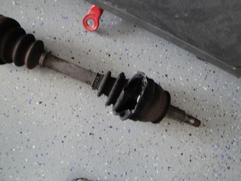 1989 Ford Taurus - A severely damaged CV axle lies on a speckled garage floor, showing a torn boot and exposed internal parts.