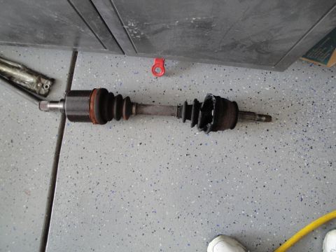1989 Ford Taurus - A damaged CV axle with a torn boot lies on a speckled garage floor.