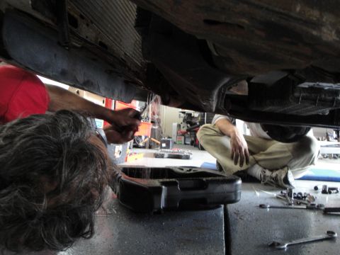 1989 Ford Taurus - Mechanics perform maintenance on the underside of a vehicle, focusing on the engine area.