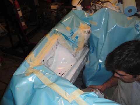 1989 Ford Taurus - A person is preparing a car's engine bay for painting by masking it with blue plastic sheeting and tape.