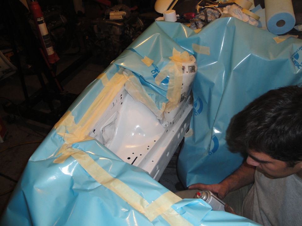 guy masking off engine bay with blue plastic and tape, holding a spray can