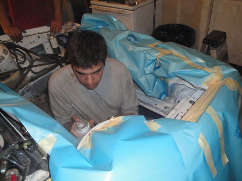 1989 Ford Taurus - A person works on a car's engine bay, which is covered in protective sheeting.