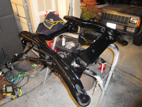 1989 Ford Taurus - A black painted suspension subframe assembly is shown on sawhorses, with a Jeep Cherokee visible in the background.