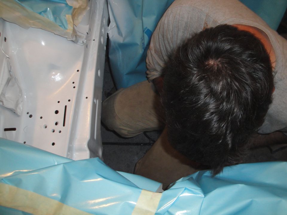 Person working inside a car's engine bay, which is covered in blue protective sheeting