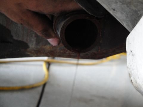 1989 Ford Taurus - Dark fluid is being drained from a pipe, possibly for maintenance or a fluid change.