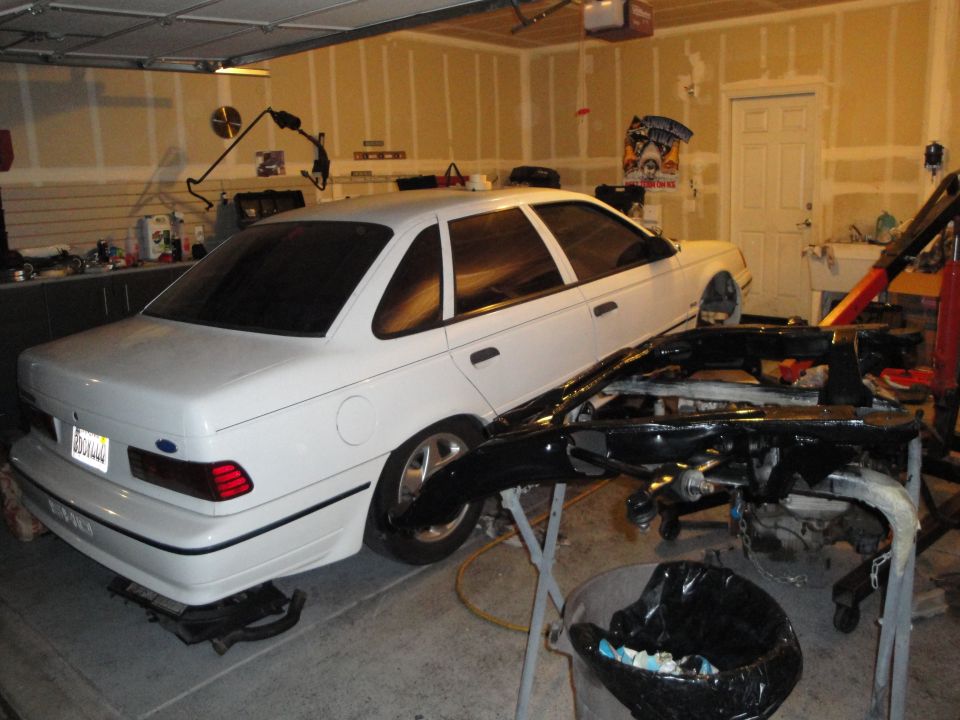 White sedan with a black bumper assembly in the foreground, parked in a garage
