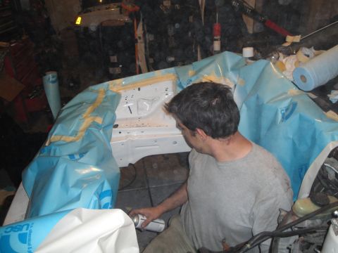 1989 Ford Taurus - A person works on a vehicle's engine bay, which is covered in protective blue sheeting and tape.