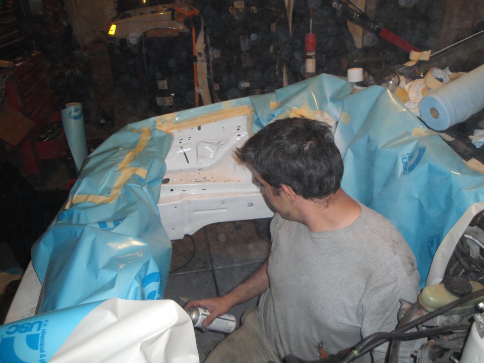 Man spraying paint in a masked-off engine bay