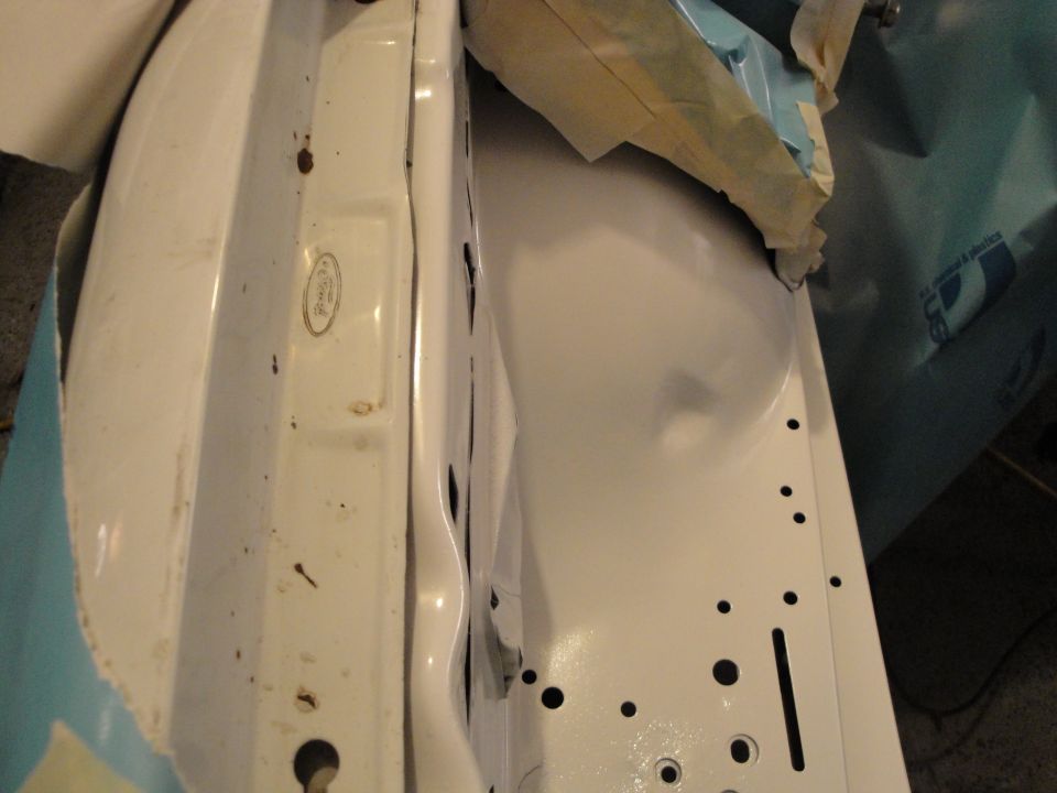 Close-up of a white car's fender and inner wheel well, showing some rust spots and freshly painted areas