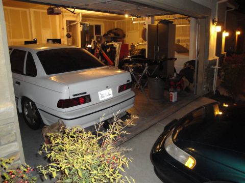 1989 Ford Taurus - A white 1989 Ford Taurus sedan is parked in a garage, with another vehicle visible in the foreground.