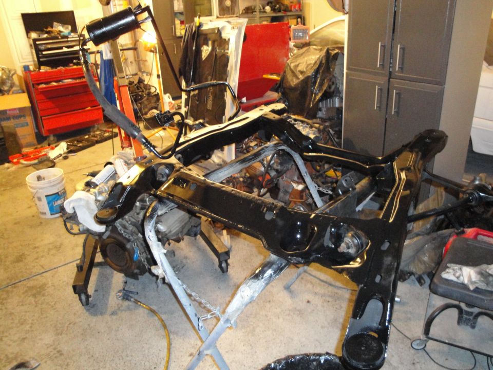 Car chassis and engine assembly on a stand in a garage. Parts are black and silver