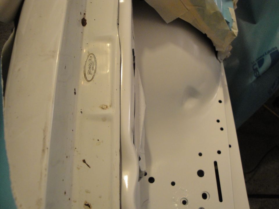Close-up of a white car part with a Ford oval emblem stamped into it