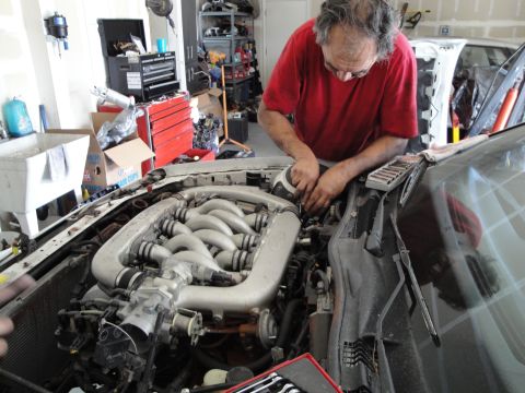 1989 Ford Taurus - Mechanic works on an engine in a cluttered garage, with tools and car parts visible.