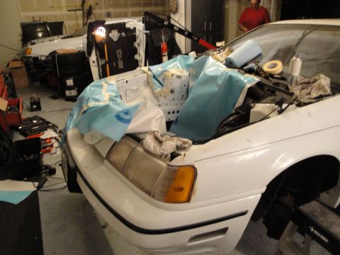1989 Ford Taurus - Front view of a 1989 Ford Taurus with its engine bay covered for work, another vehicle is visible in the garage.