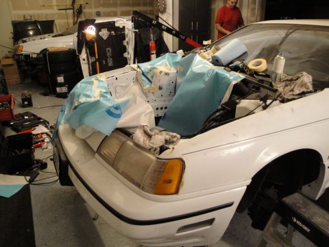 1989 Ford Taurus - The engine bay of a white 1989 Ford Taurus is covered in a blue tarp, suggesting ongoing work or an engine swap.