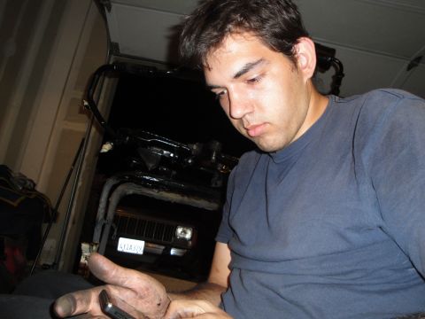 1989 Ford Taurus - A man with dirty hands checks his phone while a Jeep Cherokee sits in the background.