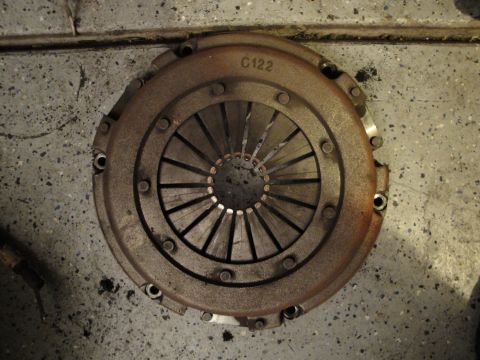 1989 Ford Taurus - A worn clutch pressure plate, marked "C122", rests on a garage floor.