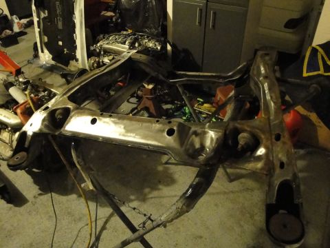 1989 Ford Taurus - A bare metal subframe is shown on a stand in a garage, likely awaiting installation or repair.