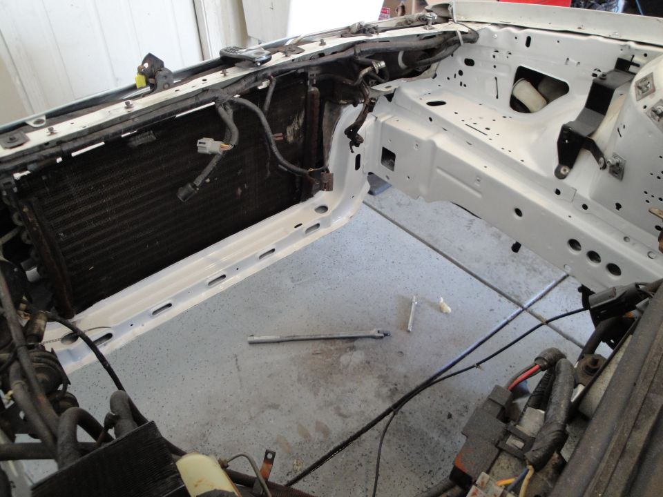 Car engine bay stripped down, showing radiator and white painted frame rails. Tools on the floor