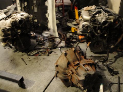 1989 Ford Taurus - Two engines and a transmission are disassembled and laid out on a garage floor, suggesting an engine swap or repair.
